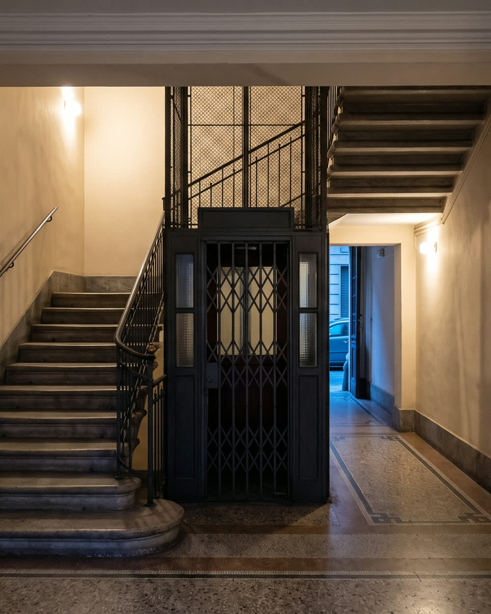 Androne di un palazzo milanese, con scala in pietra e ascensore storico.