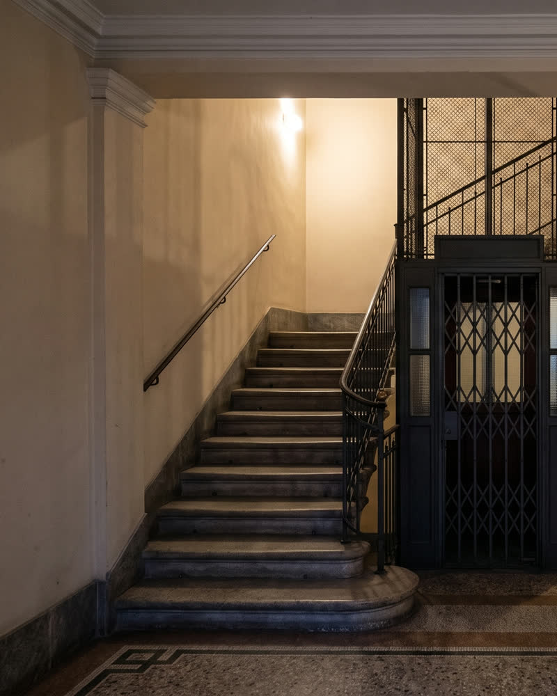 Scala in pietra di un palazzo milanese, illuminata dall'alto.